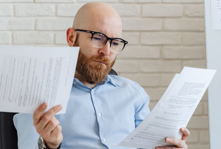 Photograph of a bald man wearing glasses and a blue shirt reviewing documents
